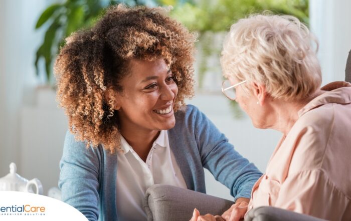 A caregiver smiles at an older client in a chair, representing the joy that can come from a healthy work-life balance.