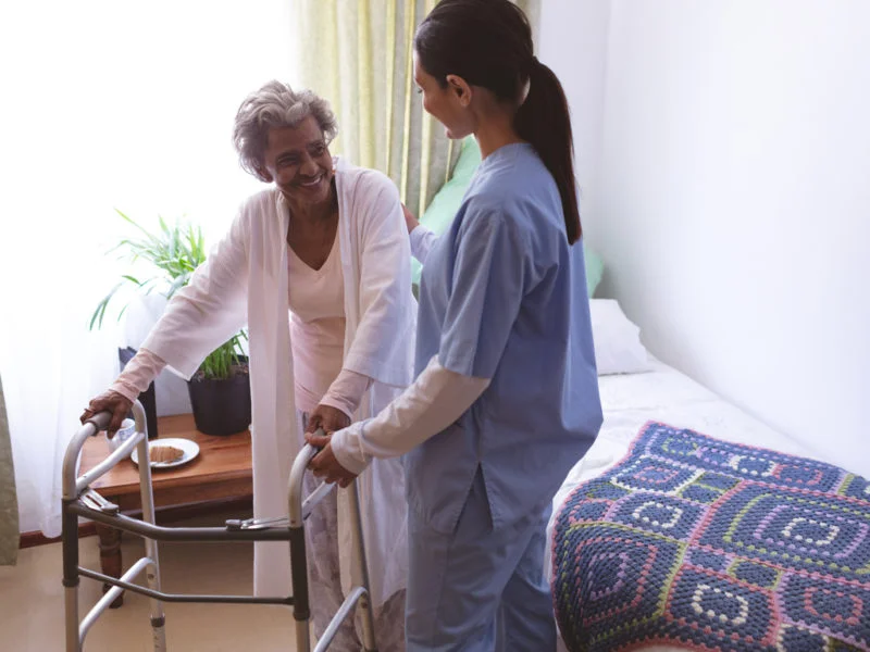 Caregiver assisting an elderly woman with a walker, representing around-the-clock care and support
